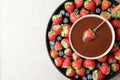 Fondue fork with strawberry in bowl of melted chocolate surrounded by different berries on light table, top view Royalty Free Stock Photo