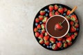 Fondue fork with strawberry in bowl of melted chocolate surrounded by different berries on light table. Space for text Royalty Free Stock Photo