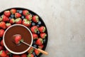 Fondue fork with strawberry in bowl of melted chocolate surrounded by different berries on light table, top view. Space for text Royalty Free Stock Photo