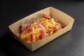 Fondue fried potatoes with cheese and crispy bacon on a black background, in a container for delivery. Deep fry potato Royalty Free Stock Photo