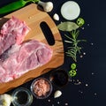 Food background. Meat on a cutting board and pepper, bay leaf, rosemary, onions, Himalayan salt, olive oil, soy sauce on a black Royalty Free Stock Photo