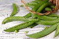 Food background. Pods of green peas scattered from a basket on a wooden table.