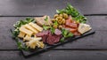 Food banner format. Assorted cheeses, sausages, smoked meat, lettuce, bread and olives on a dark flat plate of tuff on a dark Royalty Free Stock Photo