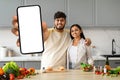 Positive young indian couple cooking at home, showing phone Royalty Free Stock Photo