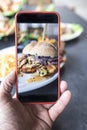 Food blogger using a smart phone taking photos of a delicious burger to share on social media Royalty Free Stock Photo