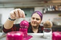 Food coloring and cake decorating concept. Praline being covered with vivid pink icing. Blurred pastry chef in the