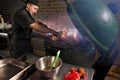 Food concept. Young chef in uniform holds hands on a grill stove. Flames erupt from under on barbecue oven