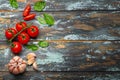 Food cooking border with cherry tomatoes, fresh green basil and garlic cloves top view on rustic colourful wooden