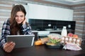 Food delivery concept. A young woman orders food using a laptop at home. On the table are milk, salads in boxes, meat Royalty Free Stock Photo