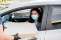 Food delivery courier gives pizza to woman in eco car. Tasty pizza with salami, cheese, tomatoes in cardoard box. Giving Royalty Free Stock Photo