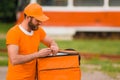 Food delivery man in orange uniform opens a food delivery bag. Royalty Free Stock Photo