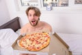 Food delivery service. Man bearded handsome guy eating cheesy food for breakfast in bed. Man likes pizza for breakfast