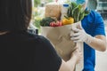 Food delivery service man in blue uniform wearing protection face mask holding fresh food set bag to customer at door home Royalty Free Stock Photo