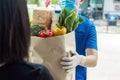 Food delivery service man in blue uniform wearing protection face mask holding fresh food set bag to customer Royalty Free Stock Photo