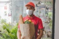 Food delivery service man with protection face mask in red uniform holding fresh food set bag Royalty Free Stock Photo
