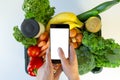 Food delivery service - woman holding smartphone in front of the box of groceries
