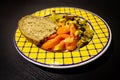 Food Dish on Black Wooden Background. Couscous, Tomato, Peanuts, Raisins, Bread. Yellow Blue Plate. Close-Up