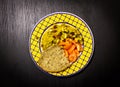 Food Dish on Black Wooden Background. Couscous, Tomato, Peanuts, Raisins, Bread. Yellow Blue Plate. Top View
