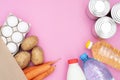 Food donation for the needy on a pink background top view. Potatoes, carrots, water, milk, oil, eggs and canned food