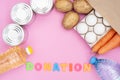 Food donation for the needy on a pink background top view. Potatoes, carrots, water, oil, eggs and canned food