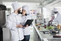 Food industry workers standing in restaurant professional kitchen while using computer to decide dinner service dish. Royalty Free Stock Photo