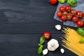 Food ingredients for spaghetti pasta with cherry tomatoes, basil leaves and garlic, black wooden background, top view with copy Royalty Free Stock Photo