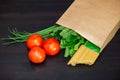 Food in a paper bag on a wooden table. Tomatoes, green onions, macaroni. Royalty Free Stock Photo