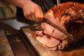 Food photography image of a cooked roast gammon or ham joint of meat with hand holding a carving knife and slicing the dinner