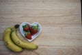 Food photography image of healthy red strawberries in a white love heart shape dish with bananas on wood background