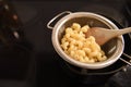 Food photography image of saucepan and sieve with cooked pasta spirals Cavatappi with black cooker hob background and space