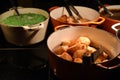 Food photography of large pans or pots filled with hot cooked crispy roast potatoes green peas and gravy on a dark surface