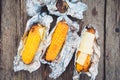 The food at the picnic. Grilled corn and cheese, wrapped in foil. Top view, on a wooden table Royalty Free Stock Photo