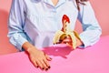 Food pop art photography. Young woman tasting banana with tomato ketchup isolated on pink background. Vintage, retro