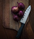 Food preparation, cooking concept: fresh raw red onions, knife on a rustic wooden cutting board background Royalty Free Stock Photo