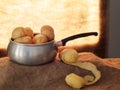 Food preparation, peeling potatoes backlit by window, rustic setting still life with saucepan, hessian aka jute.