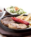 Chicken breast steak, beef steak, fried sausages, french fries, served on a hot plate, with pickles and barbecue sauce Royalty Free Stock Photo