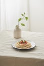 Food, spaghetti bolognese sauce in white dish and a vase of plants on a white prepared table Royalty Free Stock Photo