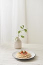 Food, spaghetti bolognese sauce in white dish and a vase of plants on a white prepared table