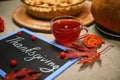 A cup of tea and a blackboard with chalk lettering Thanksgiving Day, against a blurred pumpkin pie on a linen tablecloth