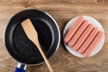 Food turner in frying pan, sausages in white plate on table. Top view