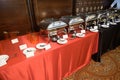 Food warmer containers laid out on red and black cloth serving tables at a restaurant