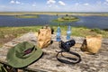 Food, water, hat, camera on the table against the background of nature. Wooden picnic table and seats near the river Royalty Free Stock Photo