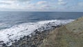 At the foot of the hill is a rocky beach. The waves of the sea come over it and foam. Above the sea is a blue sky with clouds Royalty Free Stock Photo