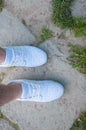 The foot of a man in white sneakers stands on stone steps in the summer