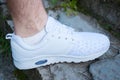 The foot of a man in white sneakers stands on stone steps in the summer