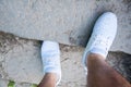 The foot of a man in white sneakers stands on stone steps in the summer. Walking in the shoes