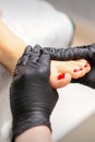 Foot massage with moisturizing and peeling cream by pedicurist hands wearing black gloves, close up. Royalty Free Stock Photo