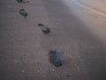 Foot prints on a black sand beach with tilt-shift blur. Surf in background. Concept for loneliness, solitude, depression