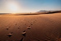 Foot prints of three travelers are swept away by the wind in the desert. Mountains and blue sea in the distance Royalty Free Stock Photo