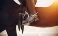 The foot of the rider, sitting on a horse, in a black boot with a spur, rests on a stirrup, illuminated by a sunlight Royalty Free Stock Photo